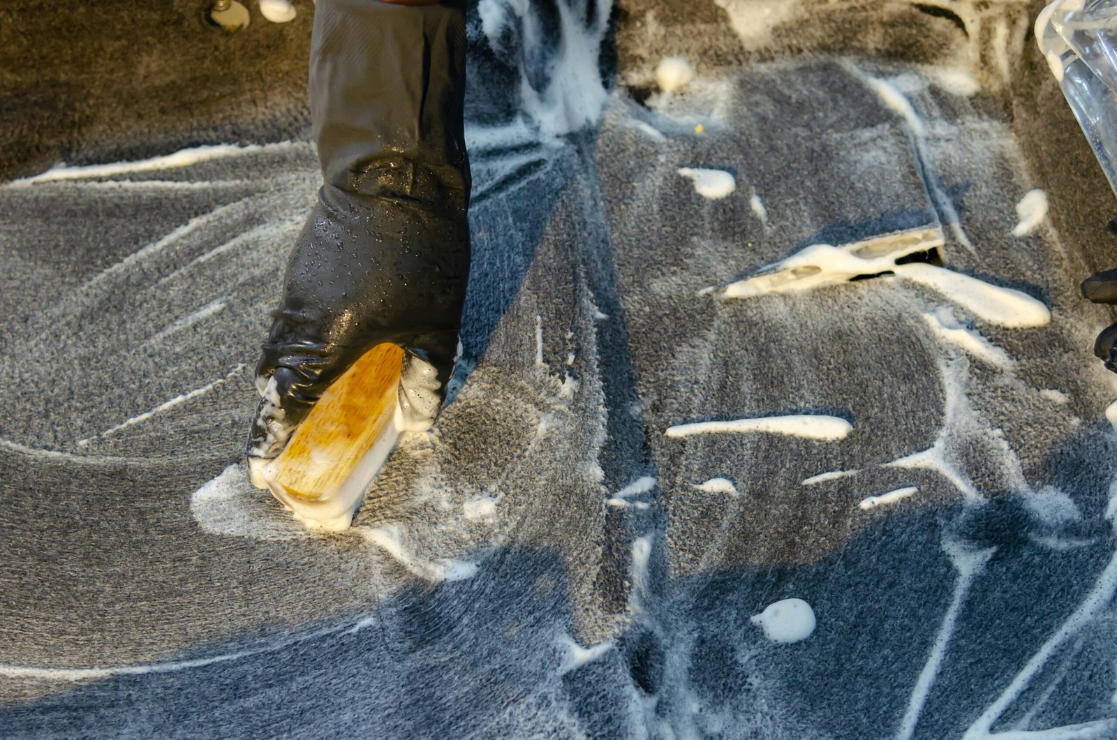 A detailed view of cleaning in progress, focusing on a gloved hand using a brush with detergent on a surface.