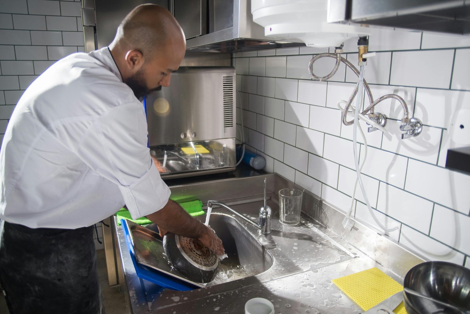 Commercial Cleaning Services Cape Town A chef cleans kitchen utensils in a stainless steel sink, maintaining hygiene standards.